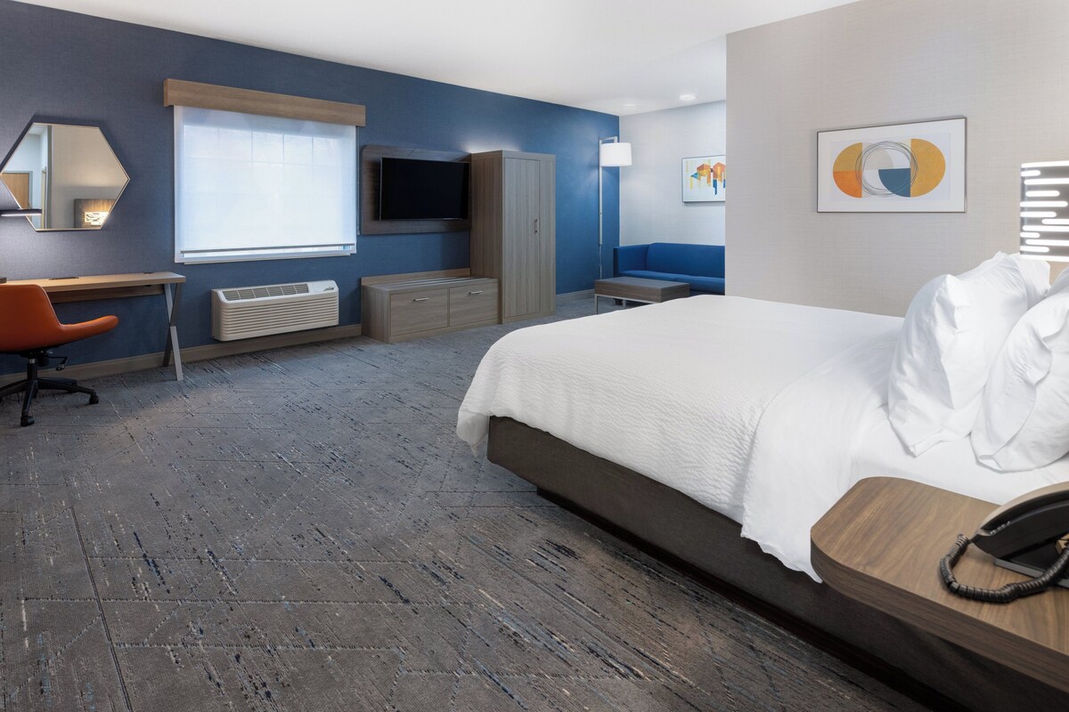 Ein Hotelzimmer mit einem Bett, einem Schreibtisch, einem Stuhl, einem Fernseher, einem Kleiderschrank und einem Nachttisch mit Telefon.