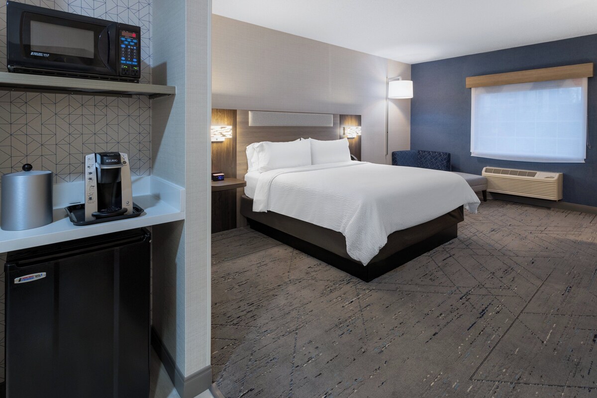 Ein Hotelzimmer mit Bett, Nachttischen, einer Mikrowelle, einer Kaffeemaschine und einer eingebauten Klimaanlage.