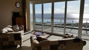 A living room with a large sliding glass door leading to a balcony with a view of the sea and wind turbines. - Powfoot Hotel (Annan)
