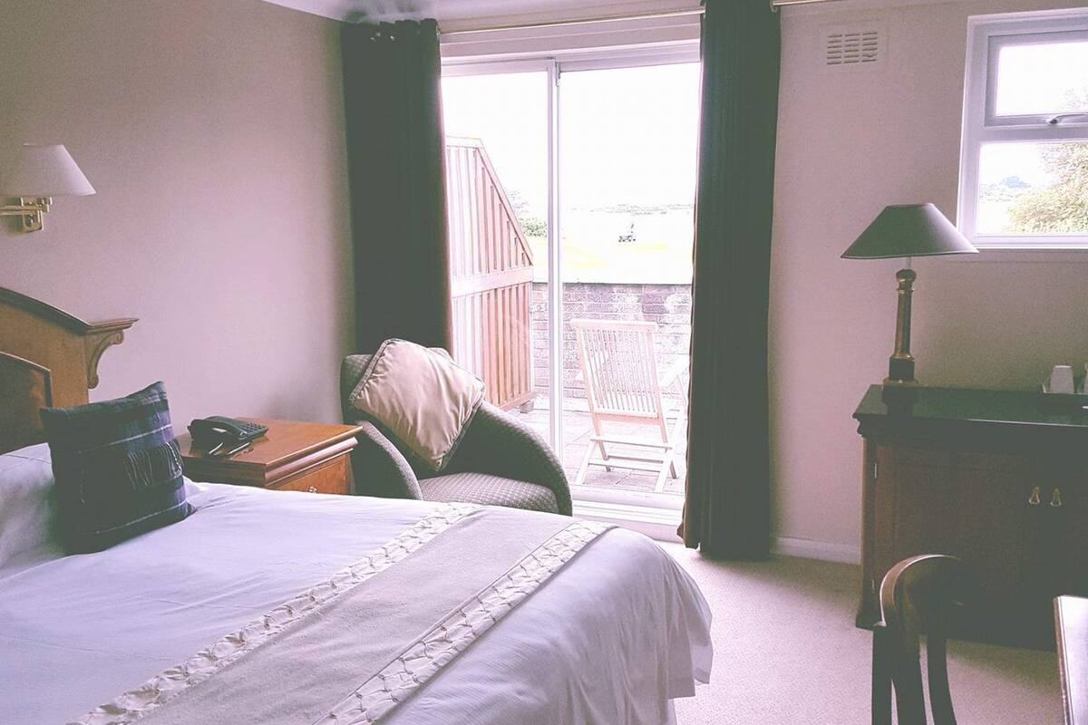 A hotel room with a large bed, a desk, a chair, and a window.