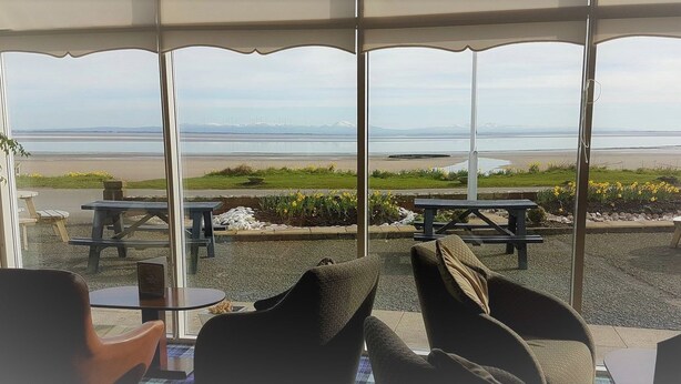 An outdoor seating area with tables and chairs, overlooking a beach and a body of water. - Powfoot Hotel (Annan)