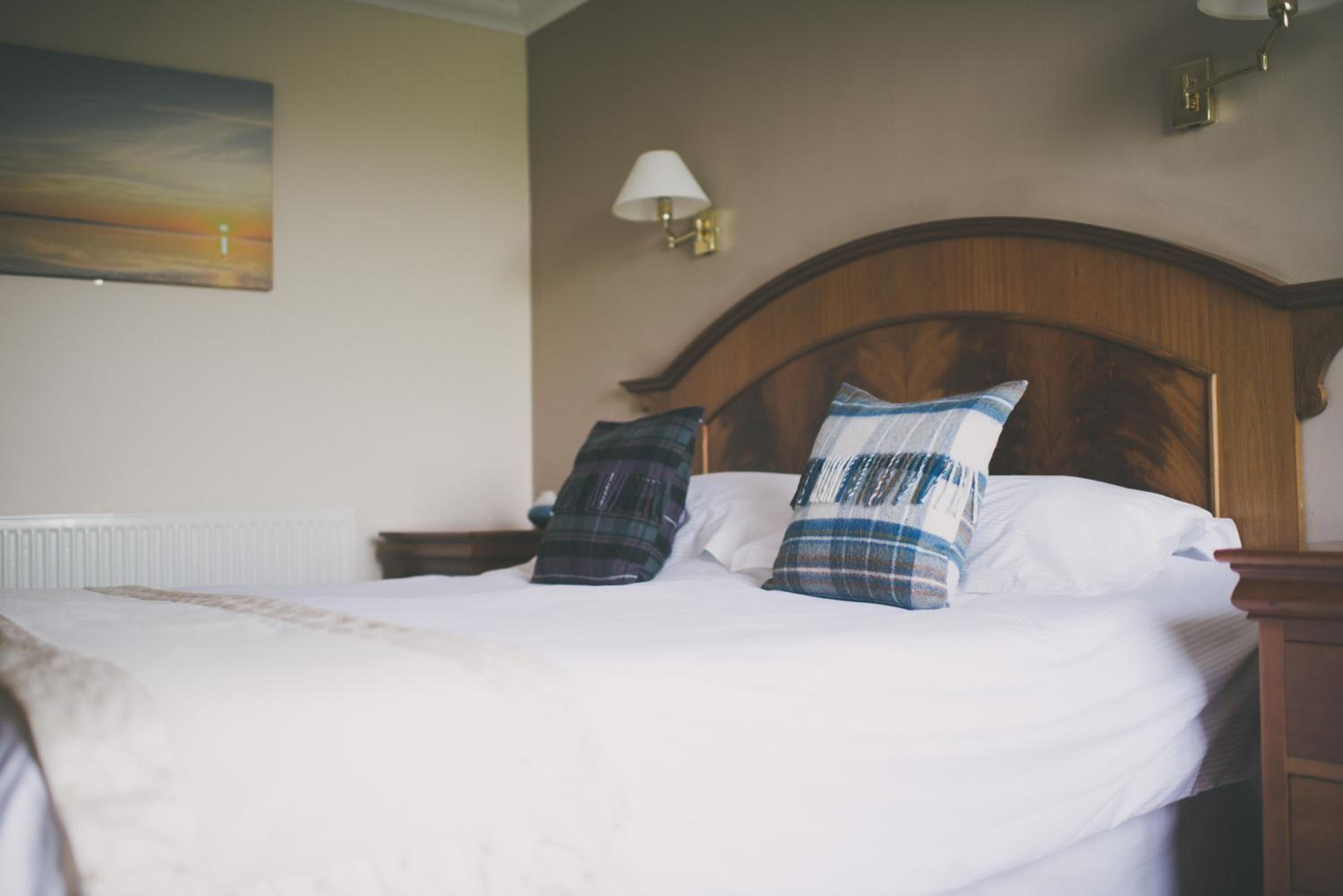 A neatly made bed with a white duvet, two plaid pillows, and a wooden headboard.