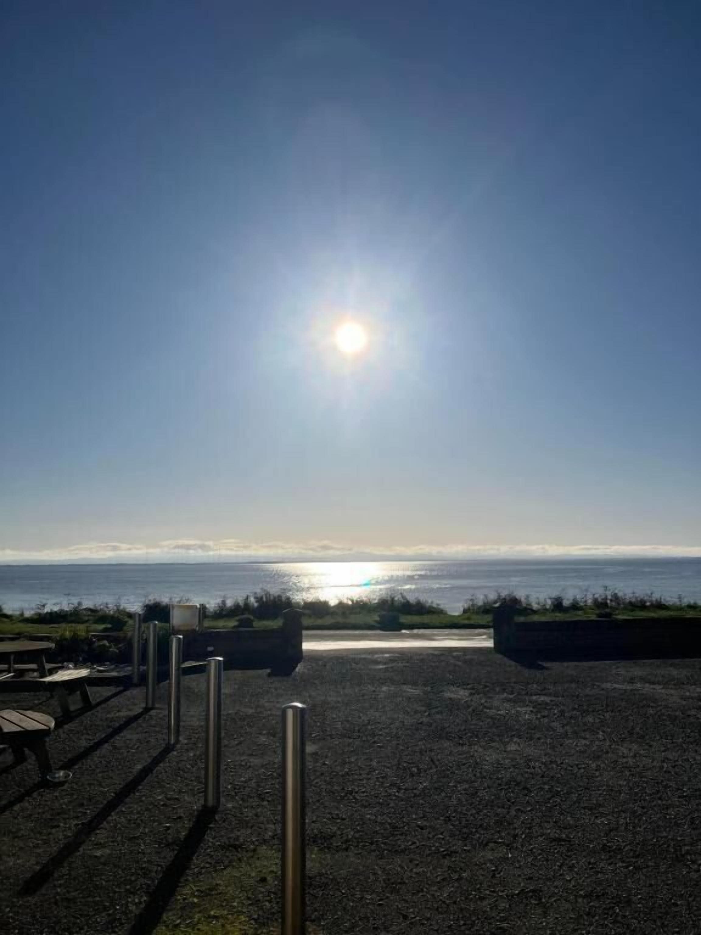 A gravel area with picnic tables and metal bollards, overlooking a body of water.