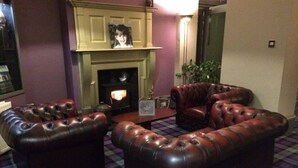 A living room with a fireplace, leather sofas, and a plaid carpet. - Powfoot Hotel (Annan)