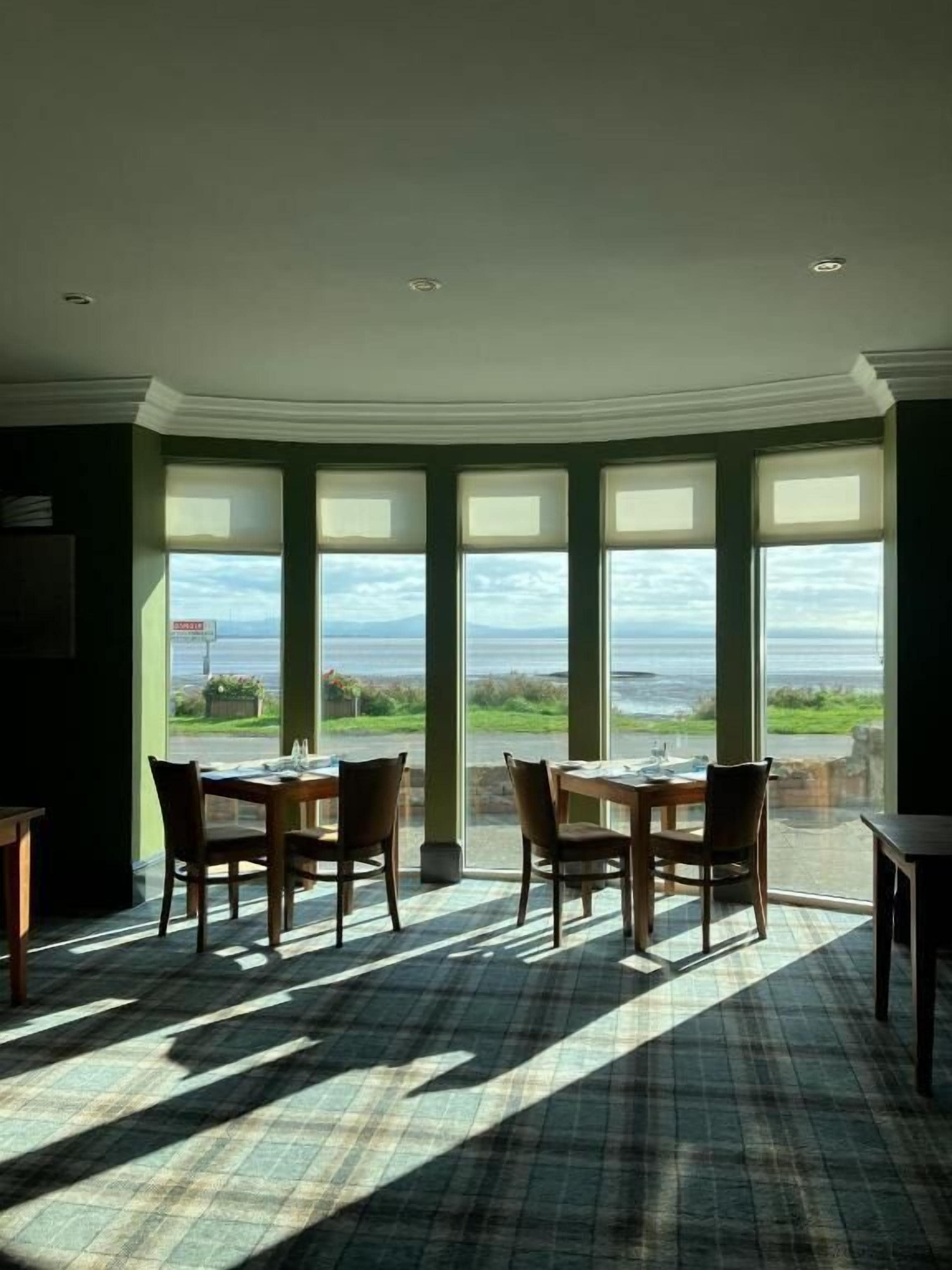 A dining area with a view of the sea, featuring a table and chairs, large windows, and a checkered floor.