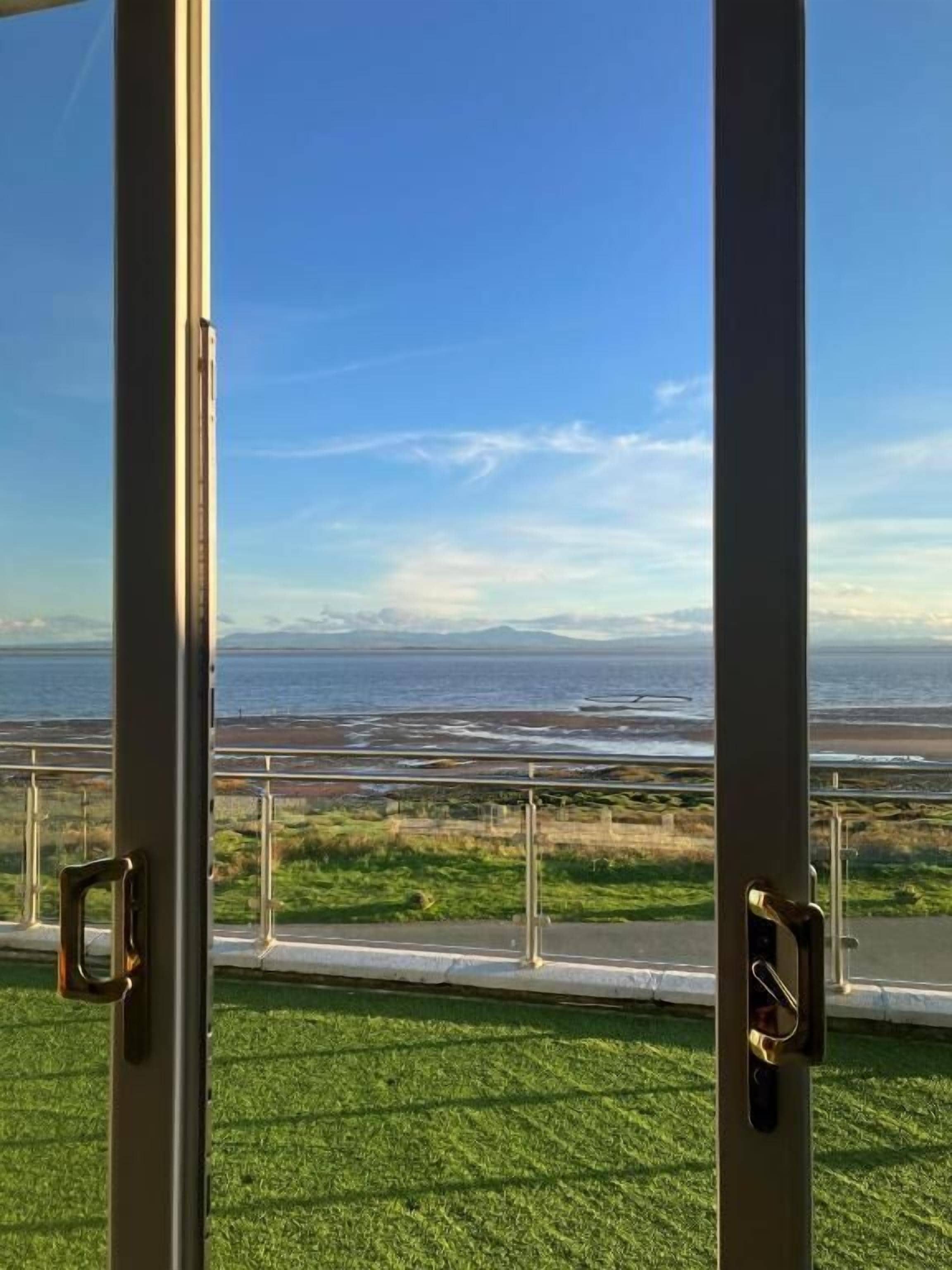 Vista a través de una ventana con marco metálico, que da a una zona cubierta de hierba y un cuerpo de agua.