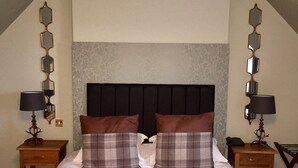 A bedroom with a large bed, two bedside tables, a headboard, and a decorative mirror on the walls. - Powfoot Hotel (Annan)