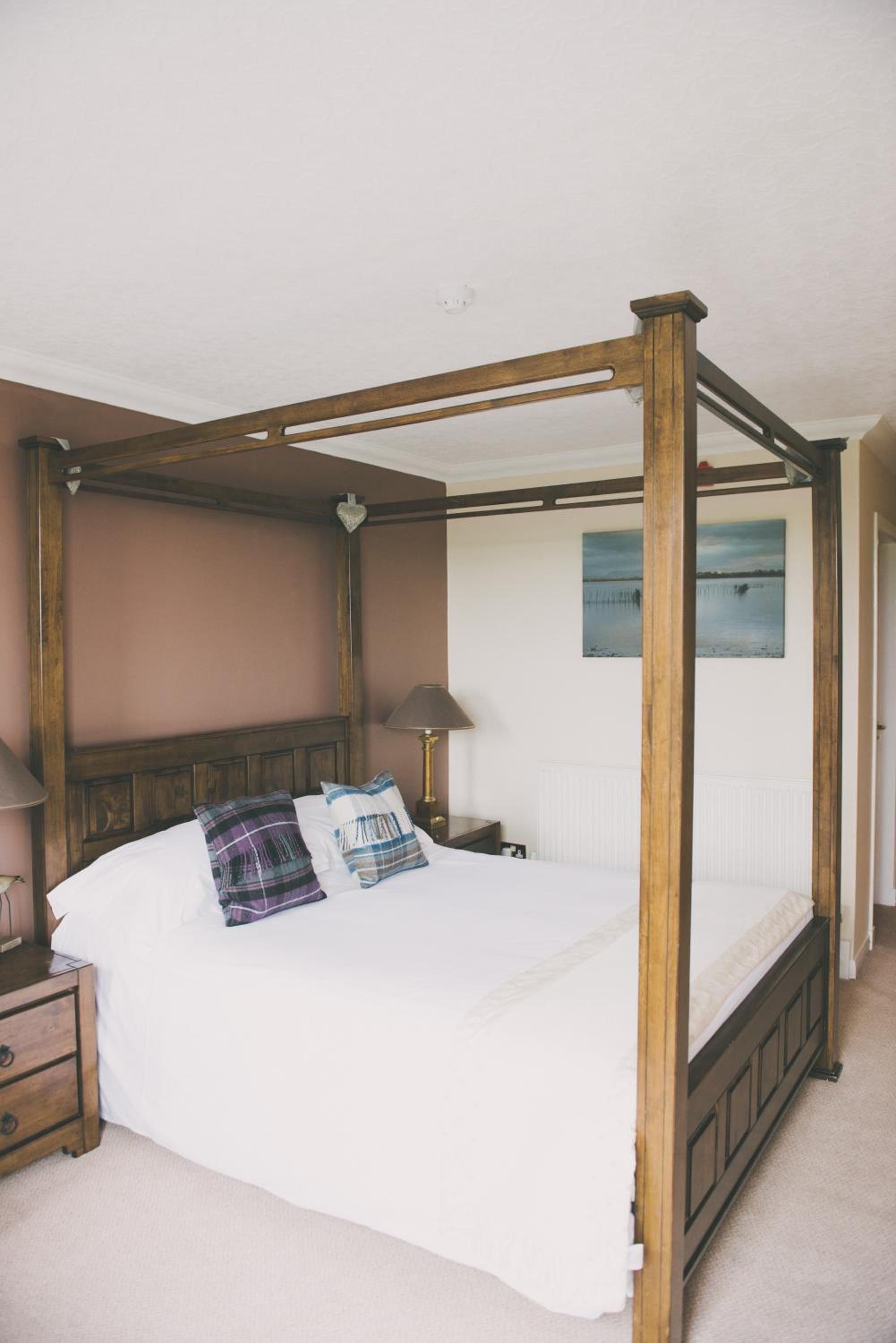 A four-poster bed with a wooden frame, white bedding, and two pillows.