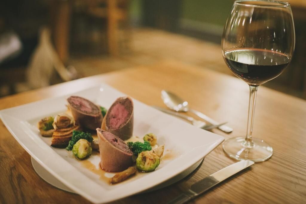 A plate of food with a glass of red wine on a wooden table.