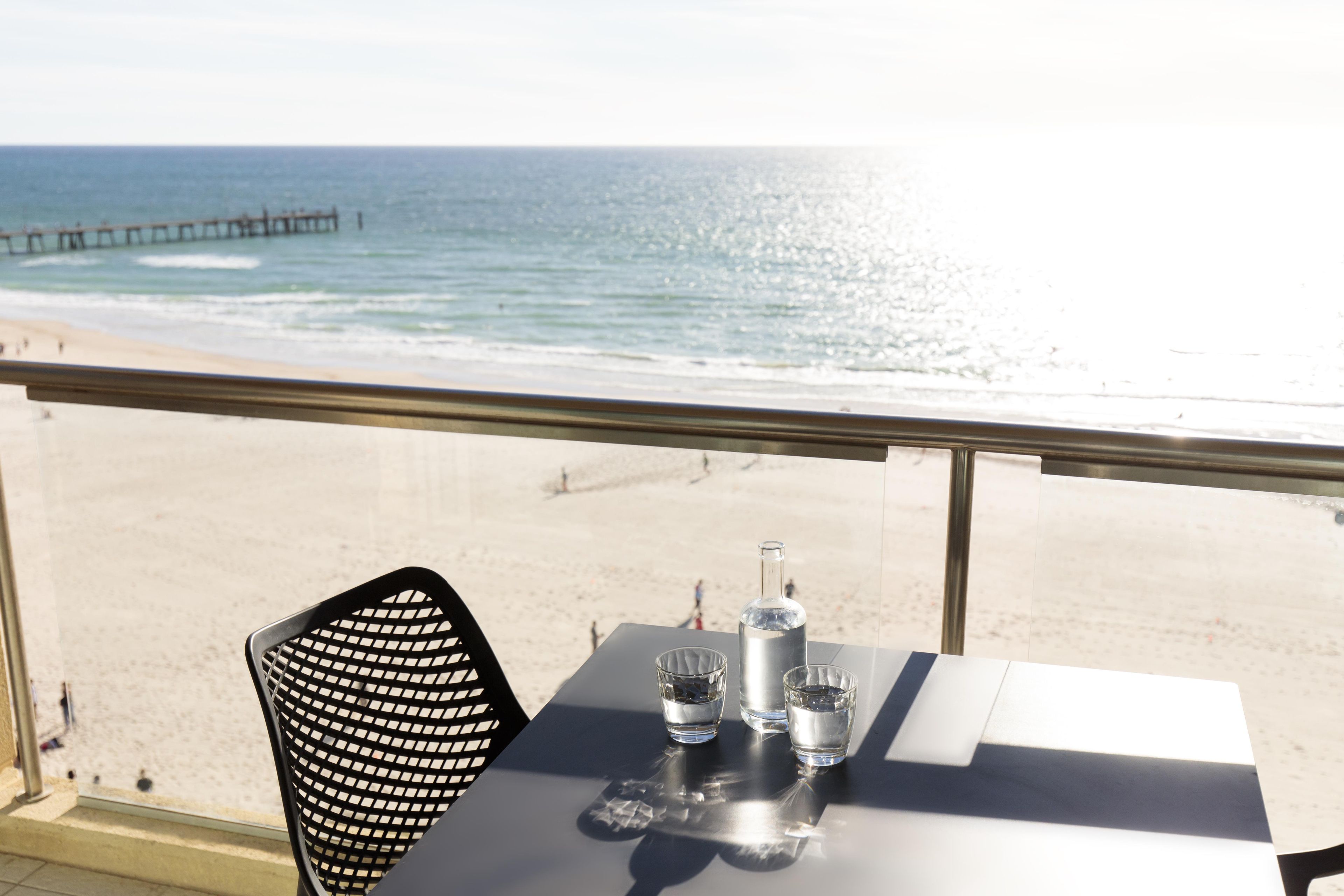 Una mesa con una botella y copas, con vista a una playa y un muelle.