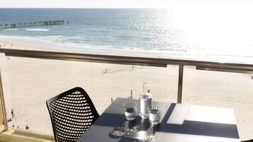 Una mesa con una botella y copas, con vista a una playa y un muelle.