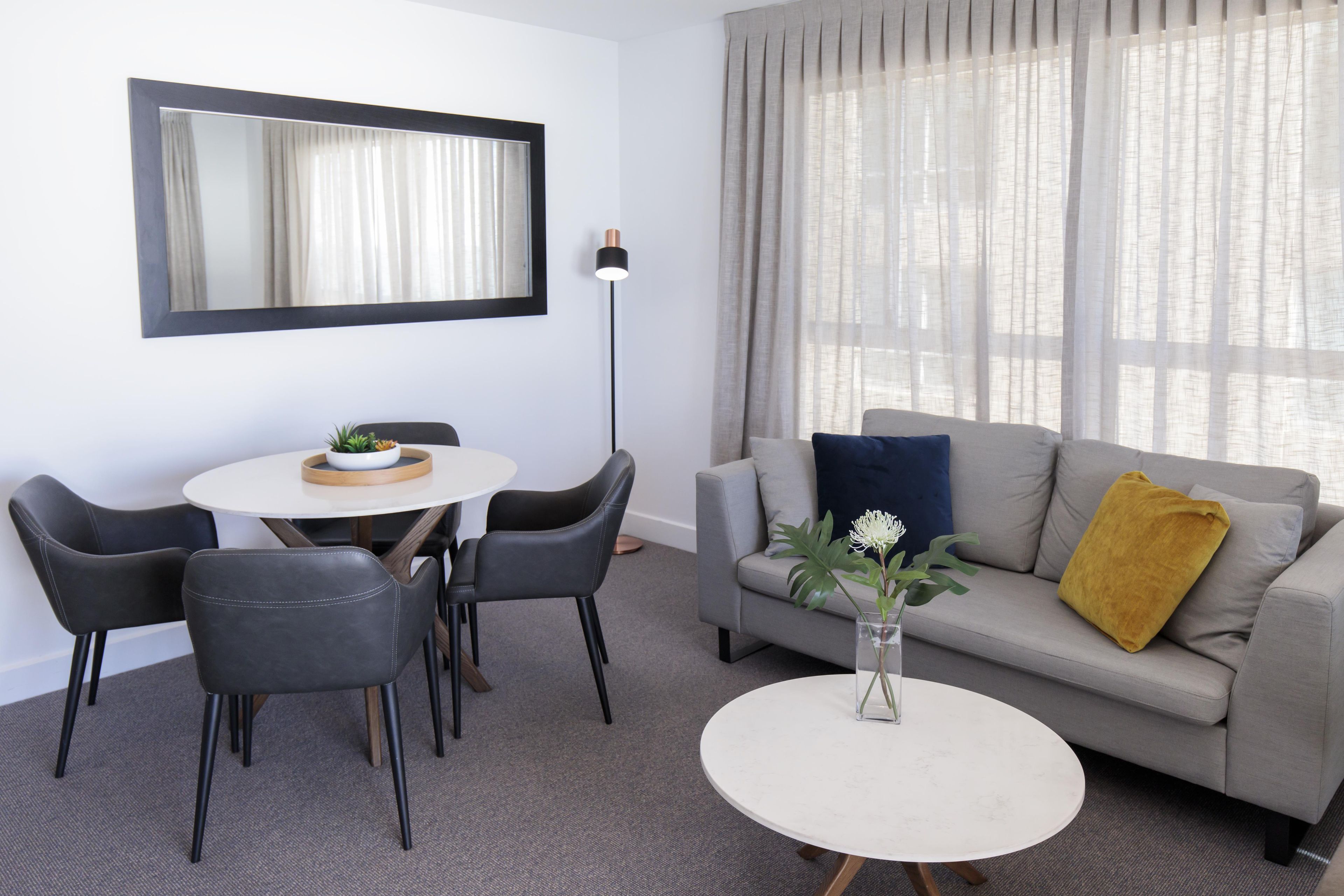 A modern living room with a grey sofa, a round coffee table, and a dining area with two chairs and a small table.