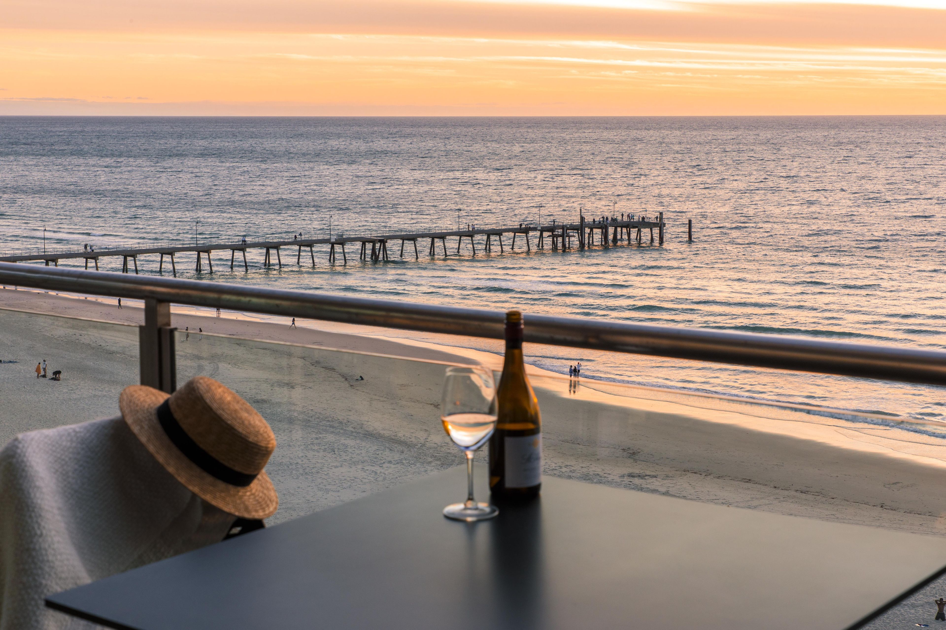 Un balcon avec vue sur la mer, une bouteille de vin et un chapeau de paille.
