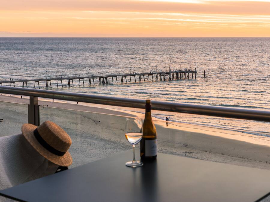 Un balcón con vista al mar, una botella de vino y un sombrero de paja.