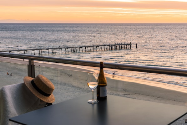A balcony with a view of the sea, a bottle of wine, and a straw hat. - Oaks Glenelg Plaza Pier Suites (Glenelg)