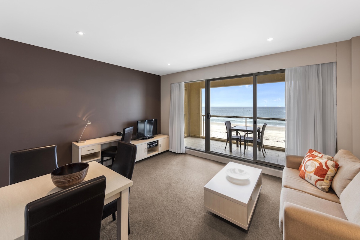 A modern hotel room with a balcony overlooking the beach, a dining area, and a seating area with a view.