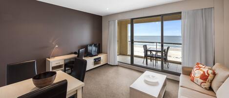 Habitación de hotel moderna con balcón y vista a la playa, zona de comedor y área de descanso.