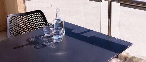 A balcony with a table, a bottle, and glasses. The view includes a beach and a pier.