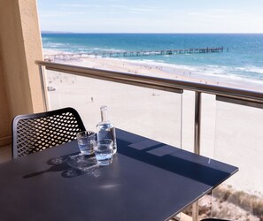 Un balcon avec une table, une bouteille et des verres. La vue comprend une plage et une jetée.