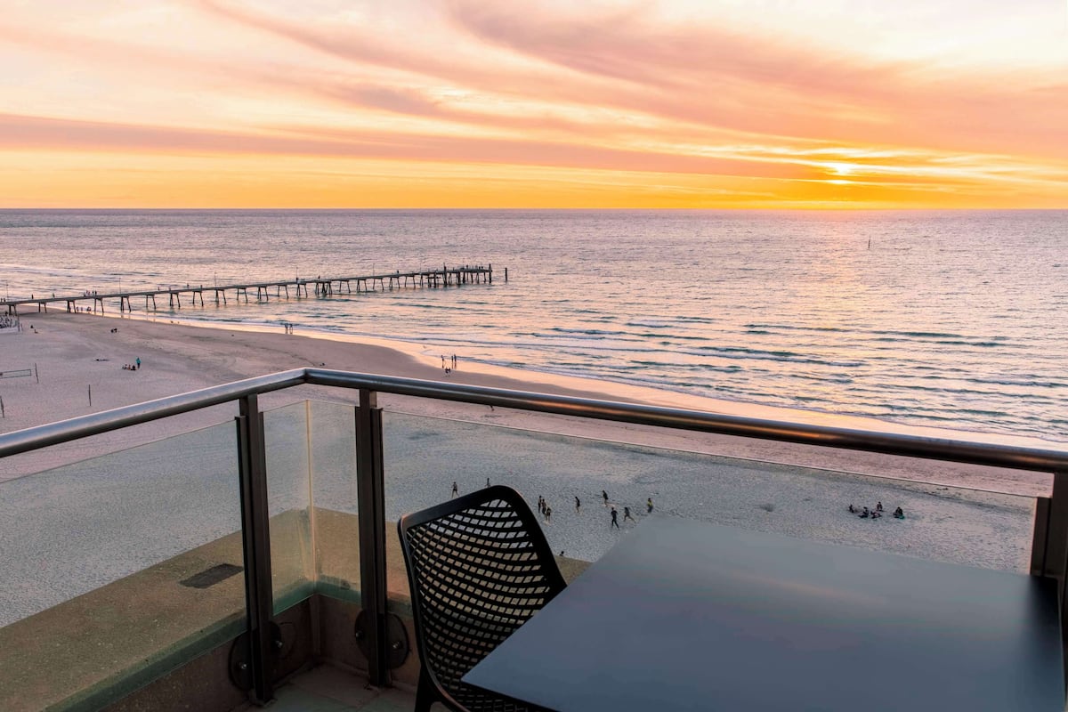 Een balkon met uitzicht op het strand en de pier tijdens zonsondergang.