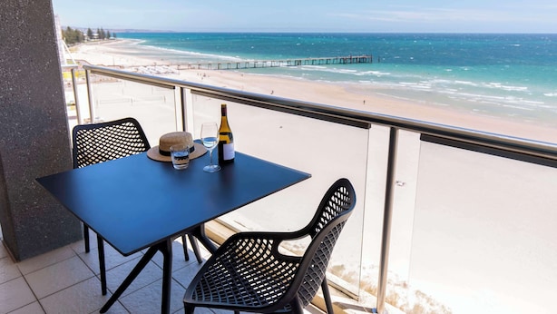 Un balcon avec une table et des chaises donnant sur une plage et une jetée.