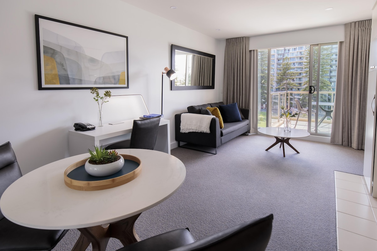 A modern living room with a round dining table, a sofa, a desk, and a large window with curtains.
