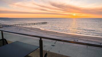 A beach with a pier extending into the water, a sandy shore, and a railing in the foreground.