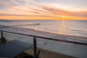 A beach with a pier extending into the water, a sandy shore, and a railing in the foreground.