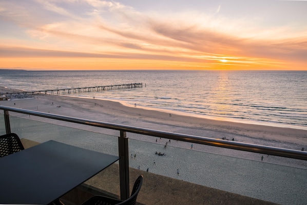 A beach with a pier extending into the water, a sandy shore, and a railing in the foreground.