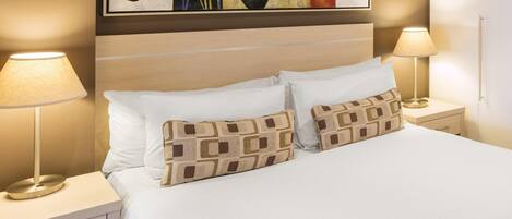 A hotel room with a bed, two bedside lamps, a nightstand, a drawer, and a painting on the wall.
