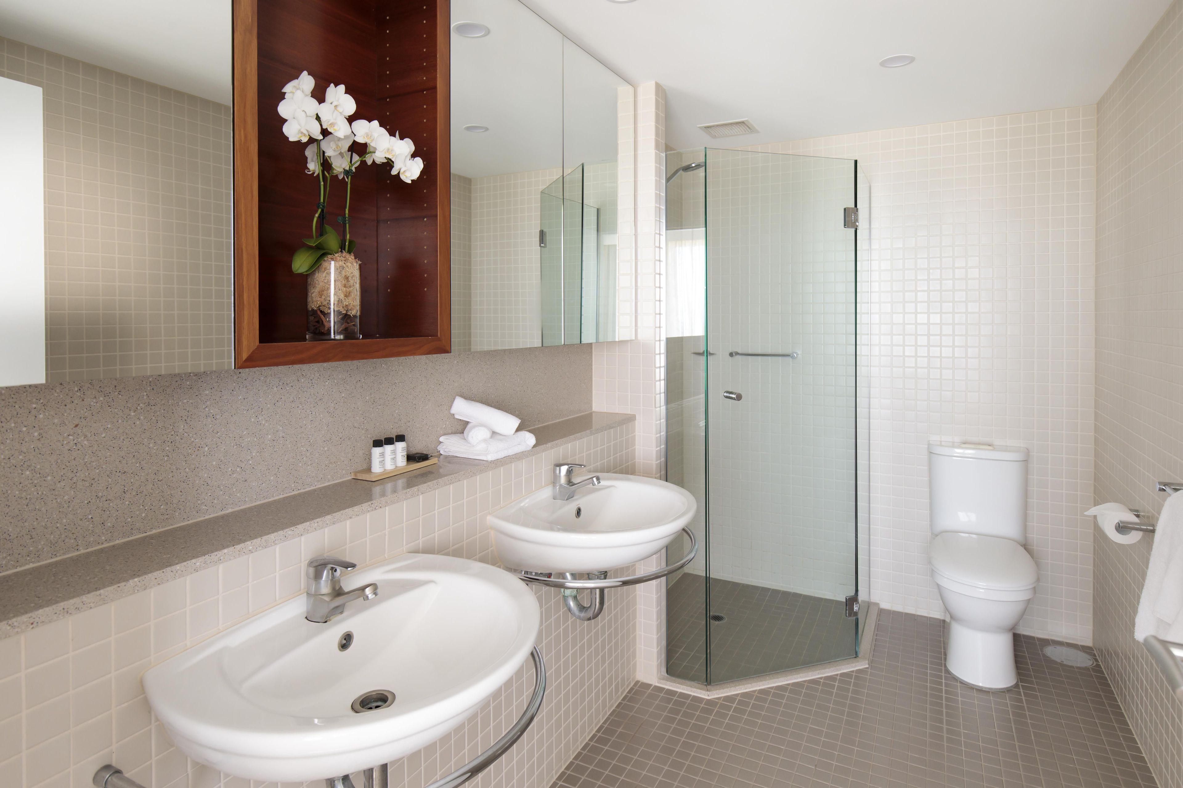A modern bathroom with two sinks, a glass shower enclosure, and a toilet.