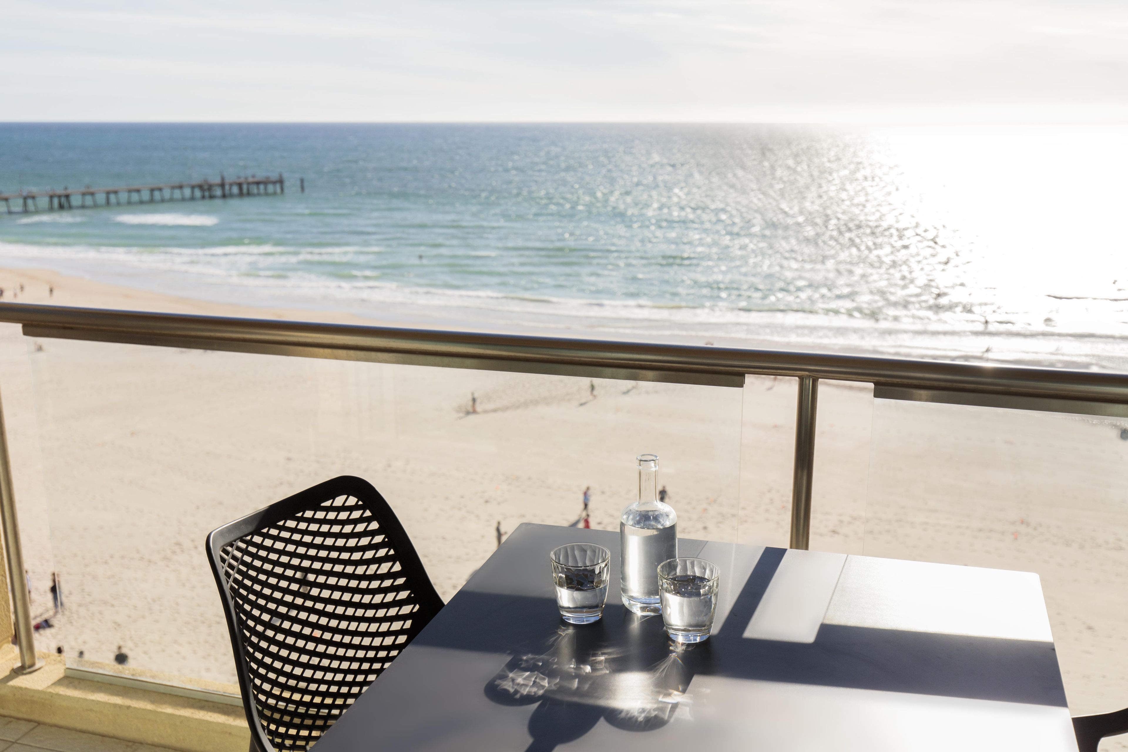 A table with a bottle and glasses, overlooking a beach with a pier.