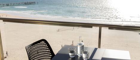 A table with a bottle and glasses, overlooking a beach with a pier.
