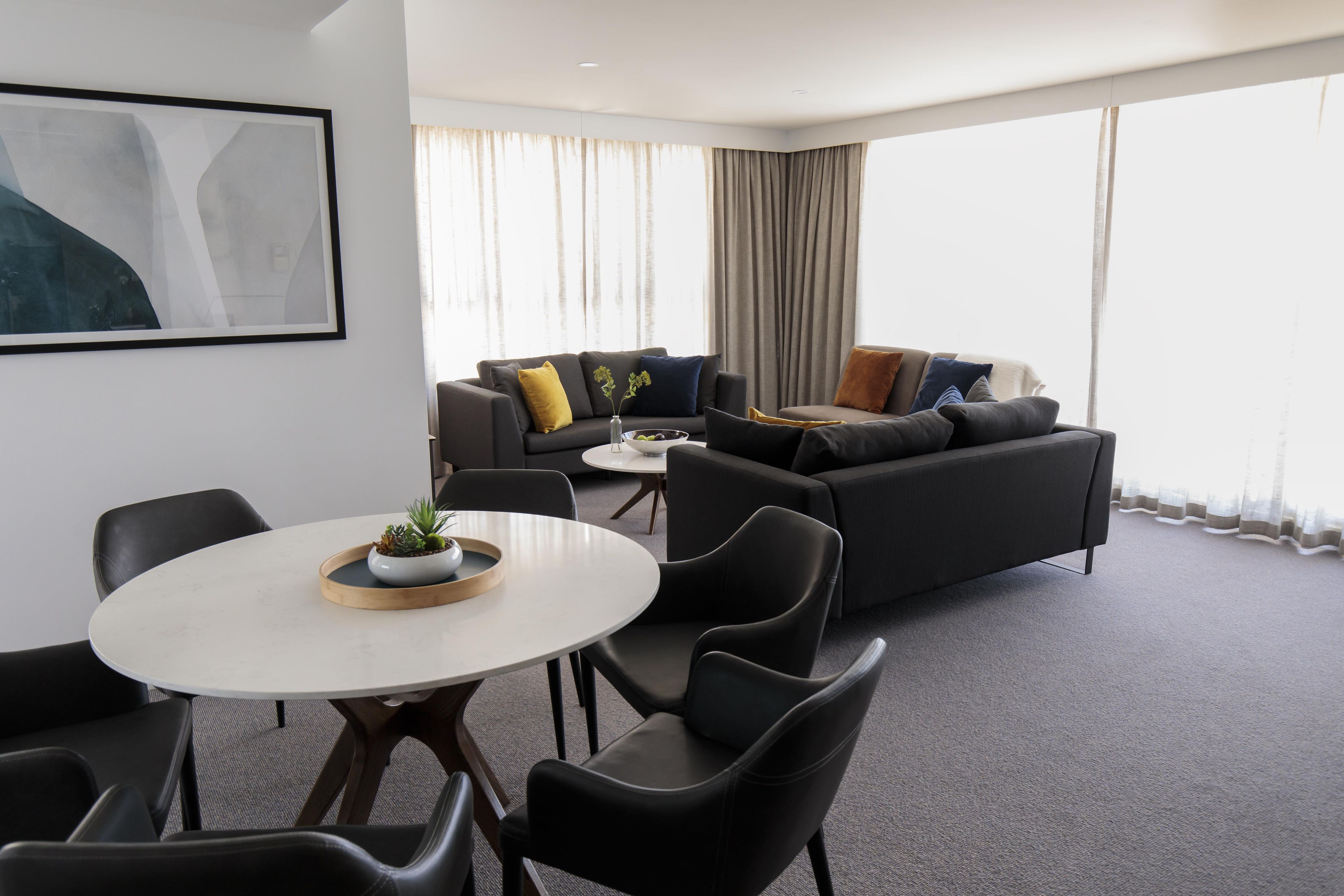 A modern hotel room with a sofa set, a dining table, and a small plant on the table.
