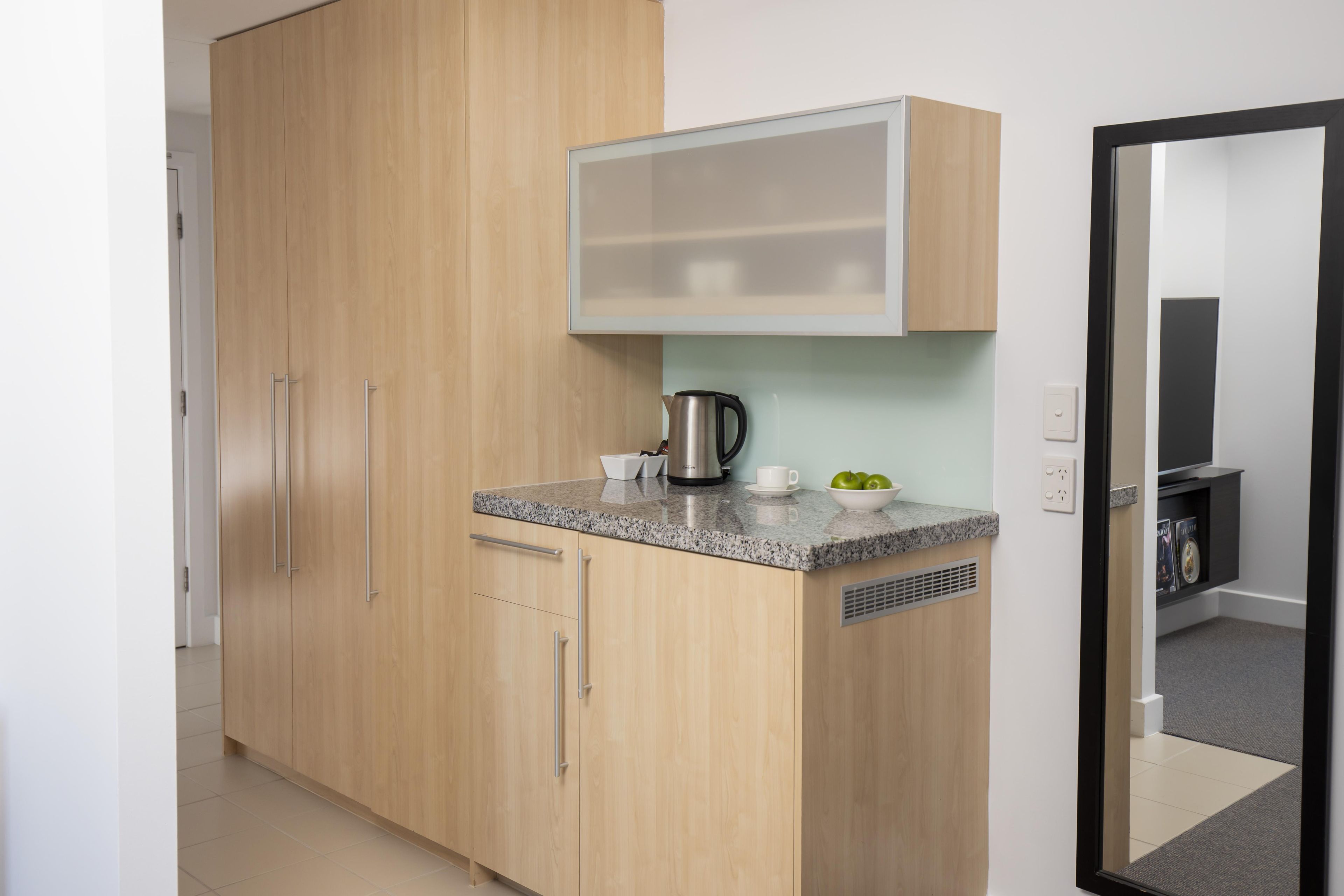 Une cuisine moderne avec des meubles en bois, un plan de travail en granit, une bouilloire et un petit bol de pommes.