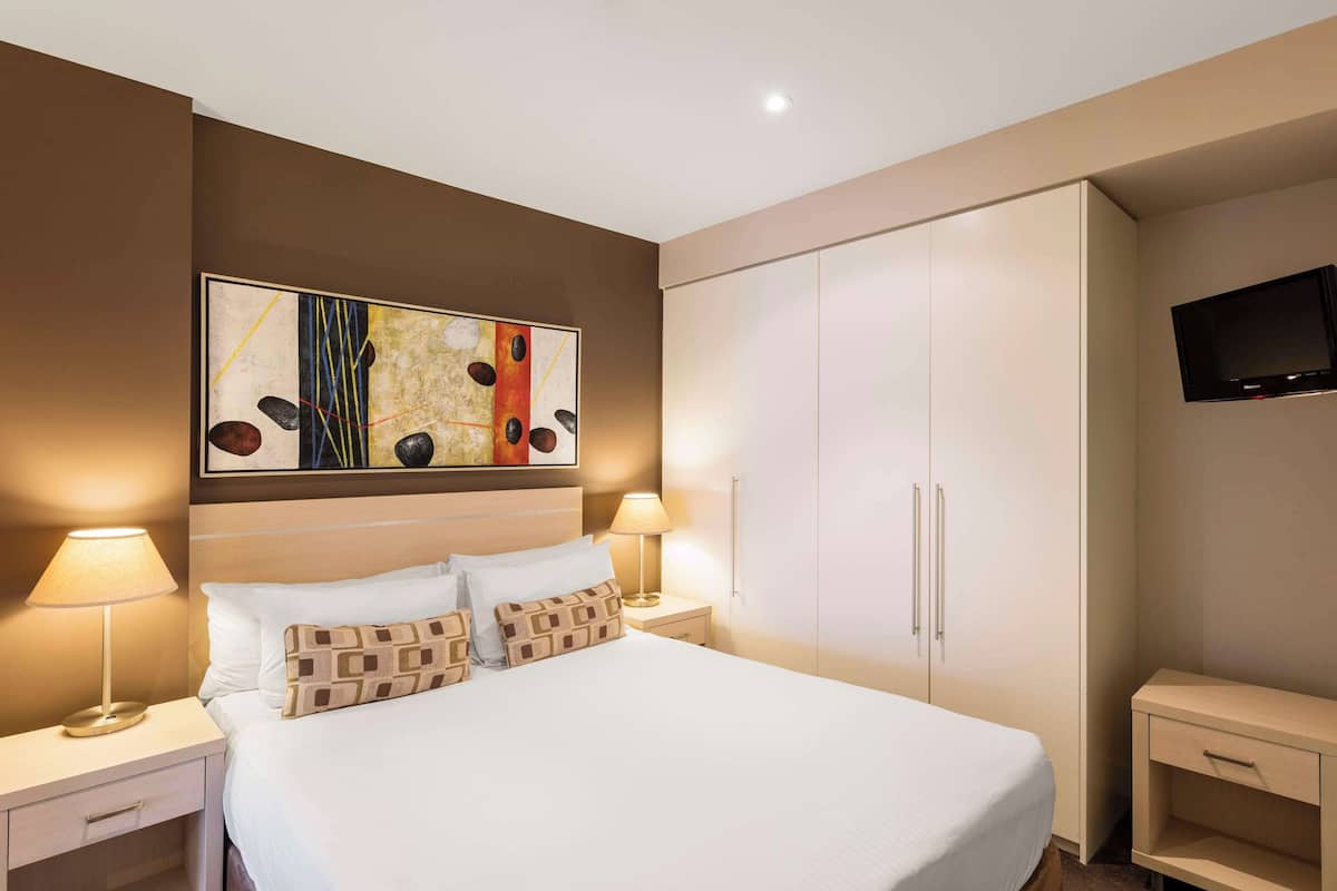 Een hotelkamer met een groot bed, twee nachtkastjes met lampen, een kledingkast en een flatscreen televisie aan de muur.