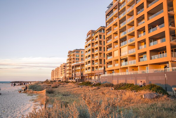 A beachfront hotel with multiple balconies, a sandy beach in the foreground, and a clear sky.