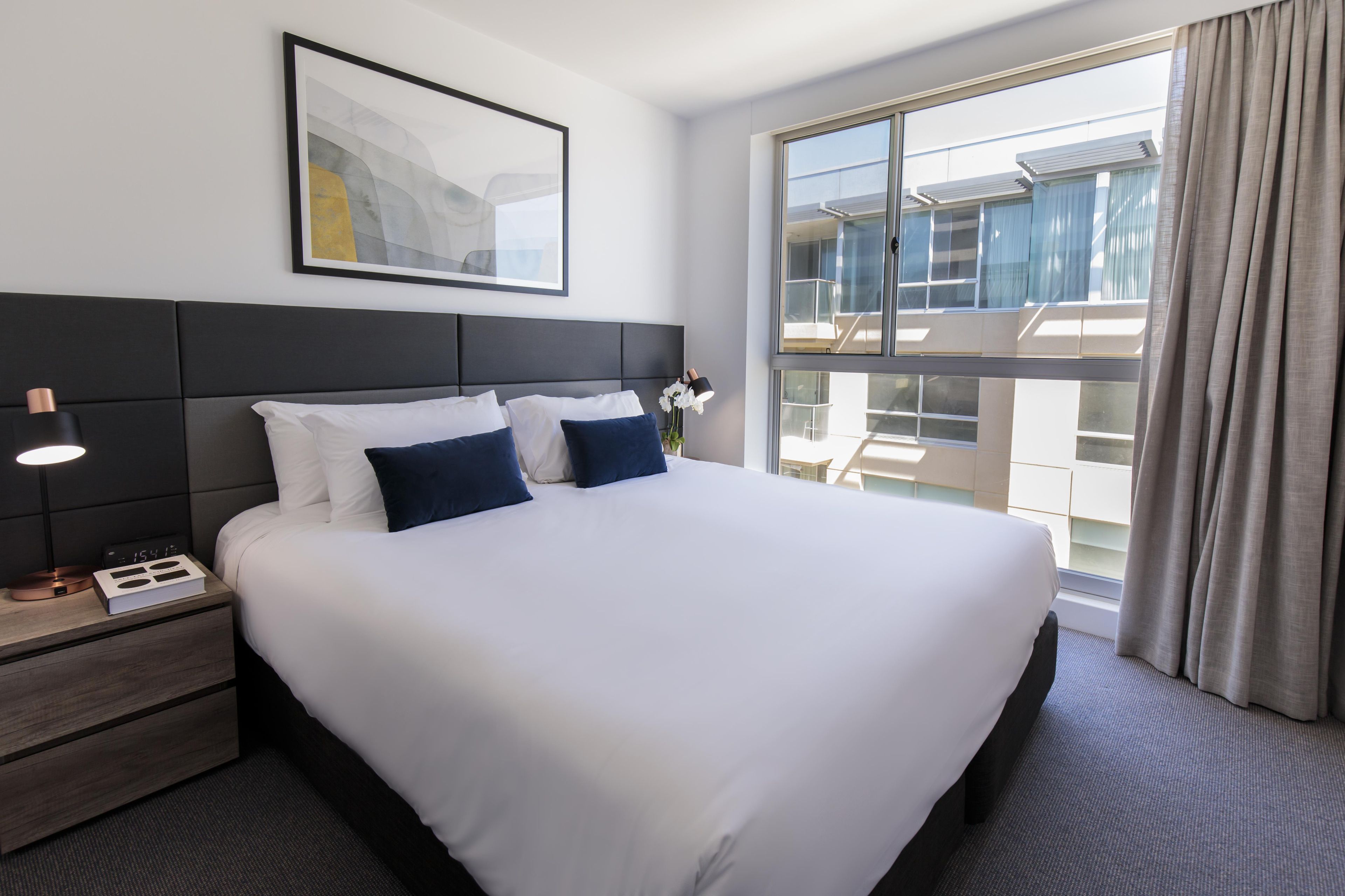 Une chambre d’hôtel avec un grand lit, une table de chevet avec une lampe, une horloge et un tableau encadré au mur.