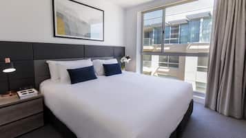 Habitación de hotel con una cama grande, una mesita de noche con lámpara, un reloj y un cuadro en la pared.