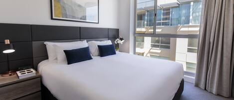 Une chambre d’hôtel avec un grand lit, une table de chevet avec une lampe, une horloge et un tableau encadré au mur.