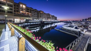 Un port de plaisance avec des bateaux amarrés, une promenade en bord de mer et un immeuble doté de balcons donnant sur l’eau.