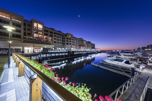 Een jachthaven met aangemeerde boten, een promenade langs het water en een gebouw met balkons met uitzicht op het water.