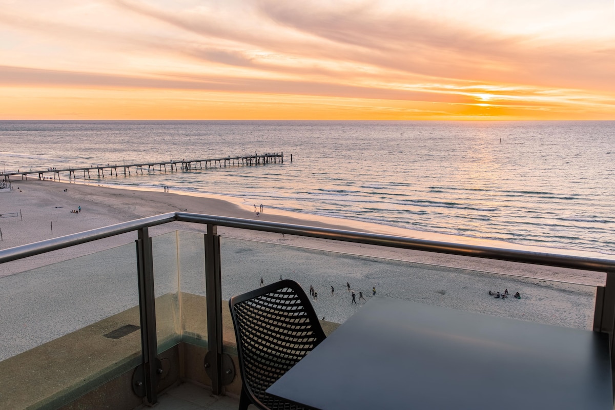 A balcony with a view of the beach and pier during sunset.