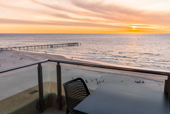 A balcony with a view of the beach and pier during sunset.