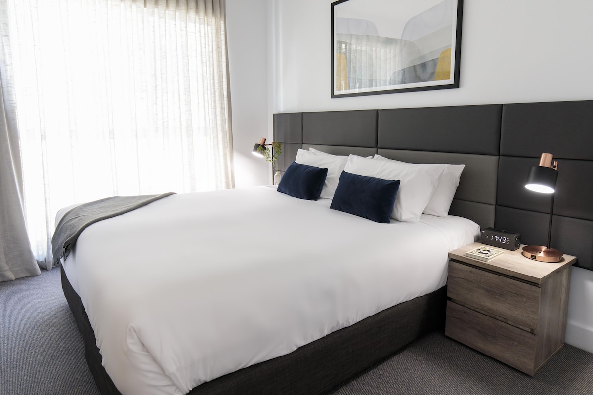 A hotel room with a large bed, bedside lamps, a nightstand, and a framed picture on the wall.