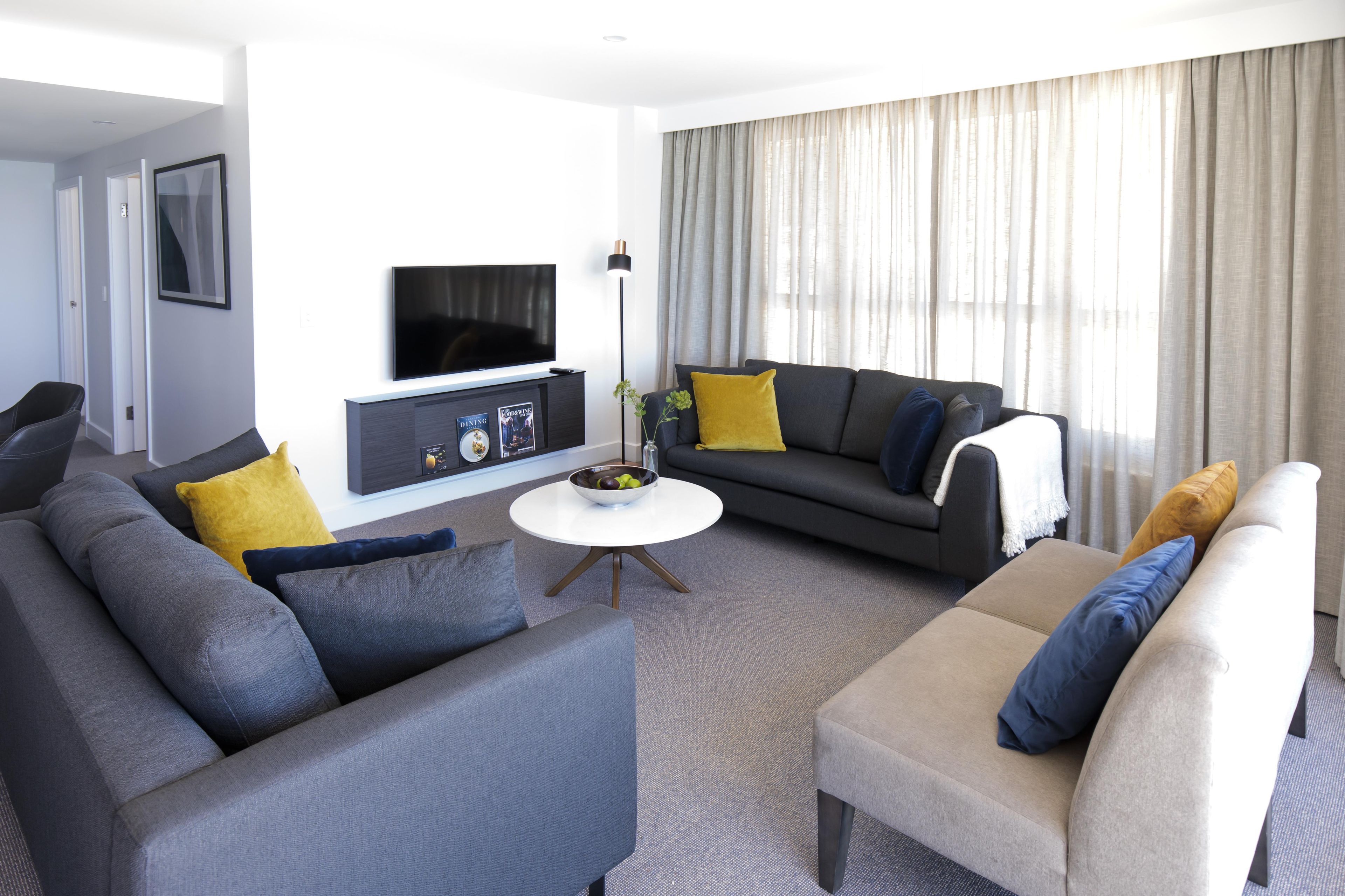 A modern living room with a flat-screen TV, a coffee table, and two sofas with cushions.