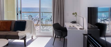 Ein modernes Hotelzimmer mit Balkon, einer Couch, einem Schreibtisch und einem Fernseher.
