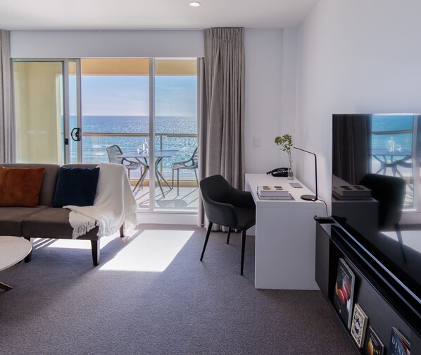Una habitación de hotel moderna con balcón, sofá, escritorio y televisión.