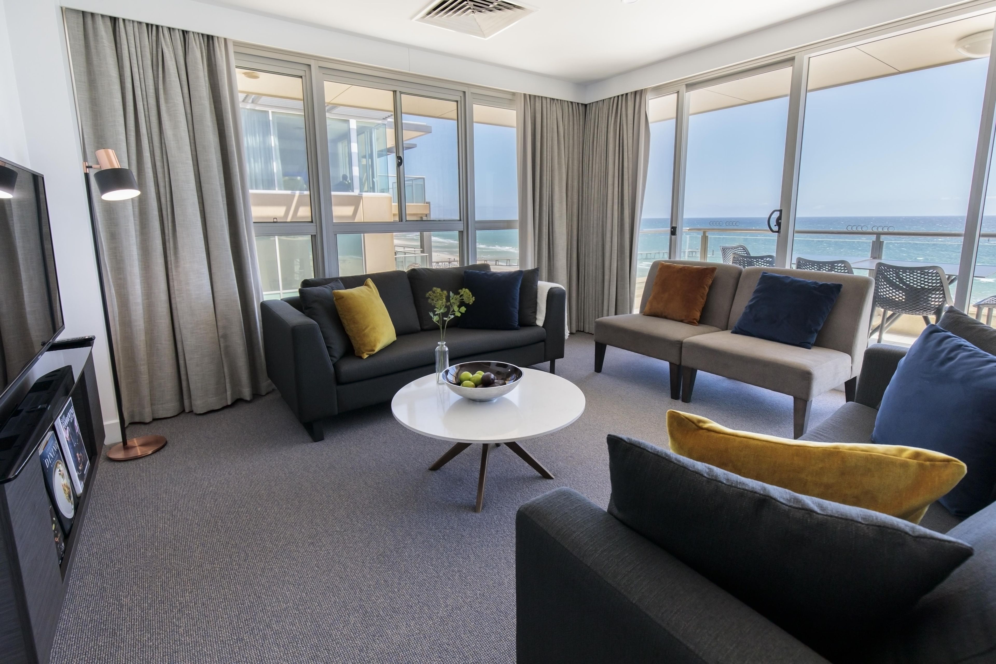 Une chambre d’hôtel moderne dotée d’un balcon, d’un ensemble de canapés, d’une table basse et d’un téléviseur.