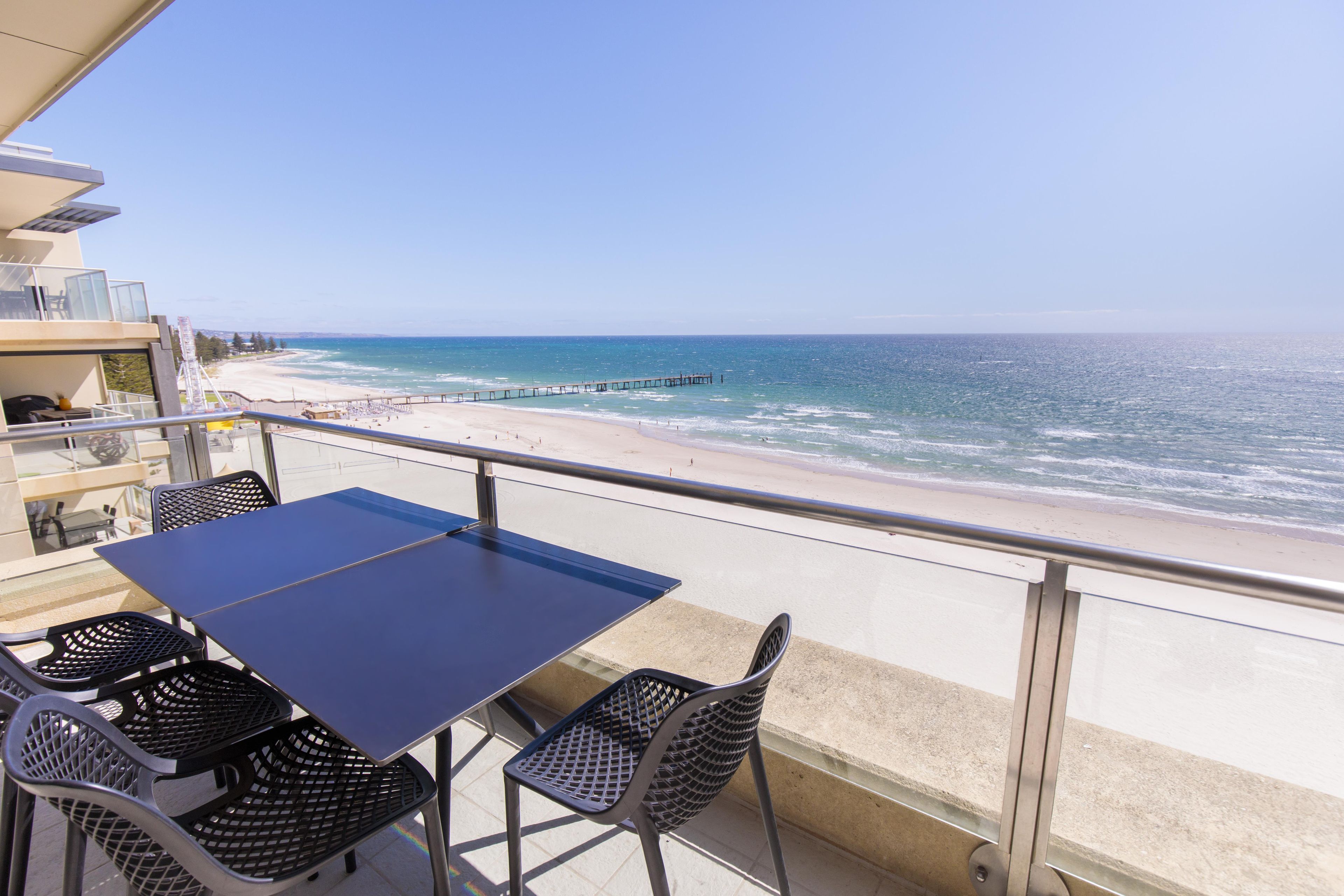 A balcony with a table and chairs overlooking a beach and ocean.